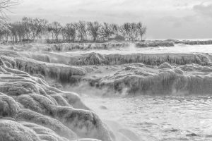 Icy rocks on Evanston’s North Shore beach with bare trees and house in background
